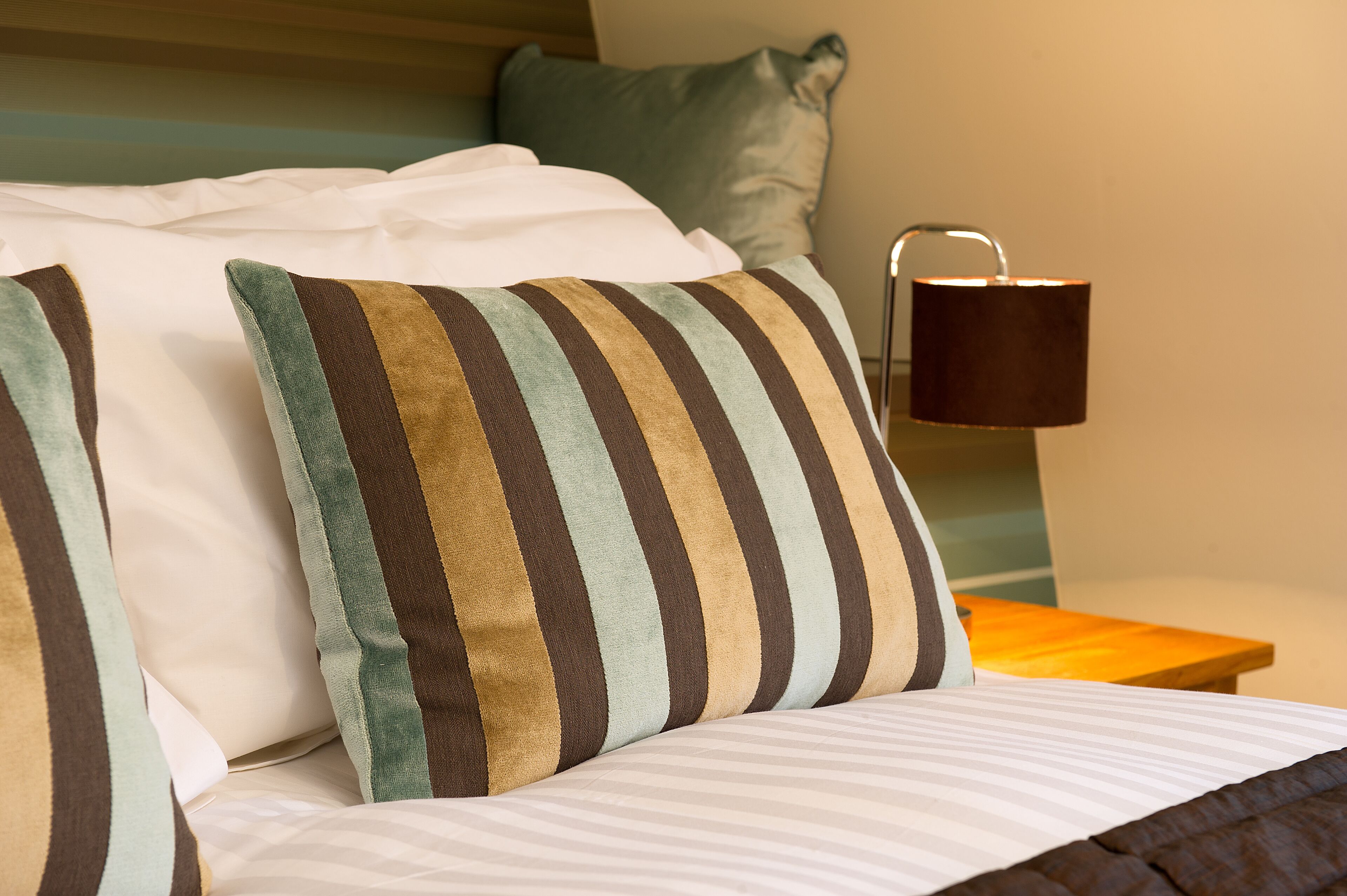 A neatly made bed with striped pillows and a bedside table with a lamp.