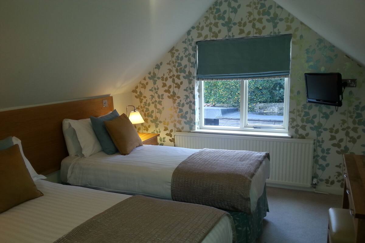 A bedroom with two beds, a window with a view, a desk, and a television.