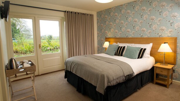 A bedroom with a bed, bedside tables, a window with curtains, and a view of greenery outside. - The Marquess Of Exeter (Oakham)