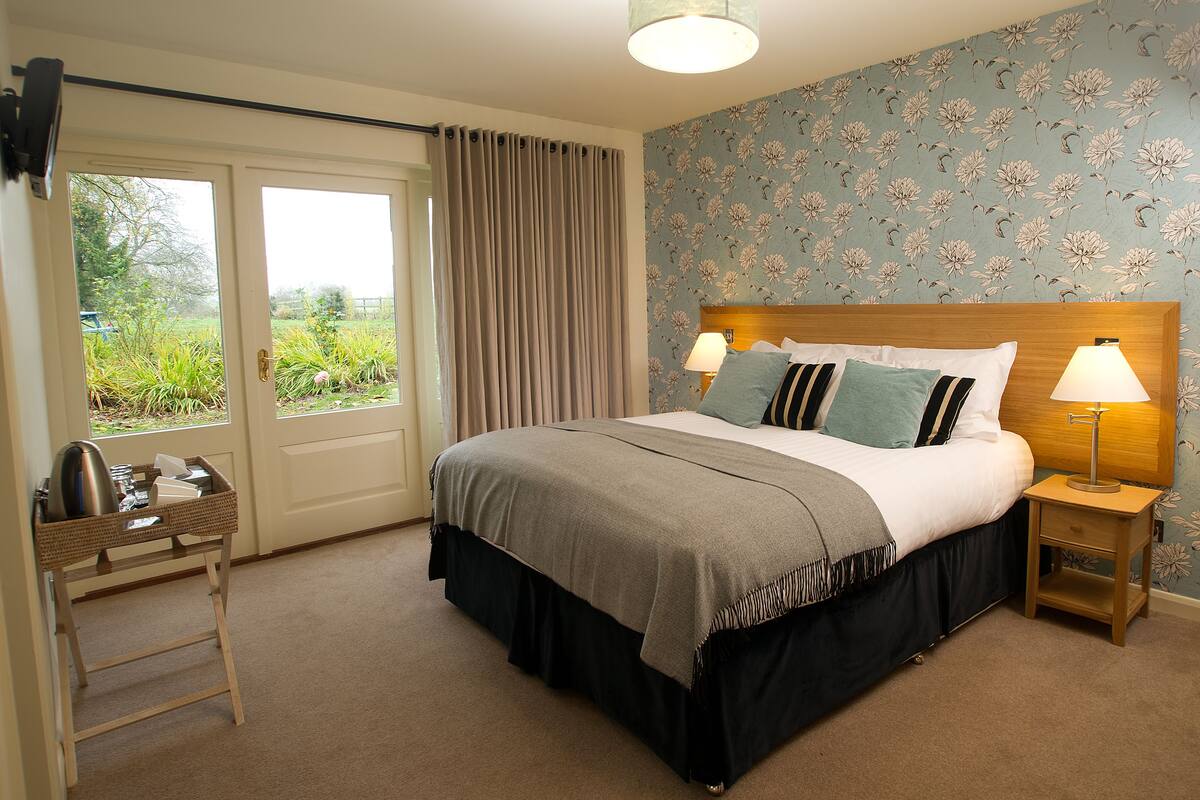 A bedroom with a bed, bedside tables, a window with curtains, and a view of greenery outside.