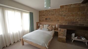 A bedroom with a stone fireplace, a bed with a wooden headboard, and a large window with sheer curtains.