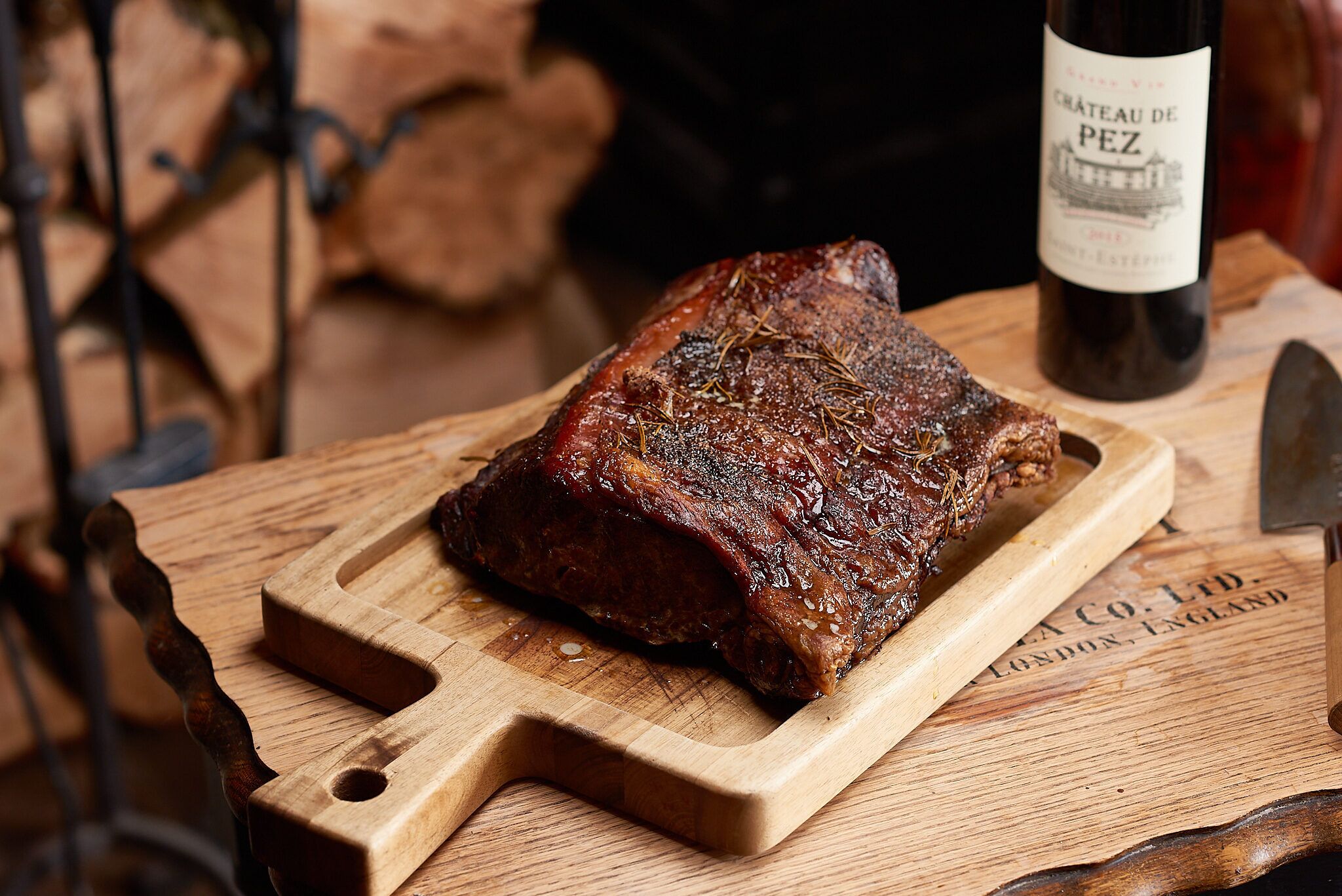 Une planche à découper en bois sur laquelle se trouve un morceau de viande cuit, une bouteille de vin et un couteau.