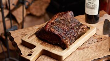 Une planche à découper en bois sur laquelle se trouve un morceau de viande cuit, une bouteille de vin et un couteau.