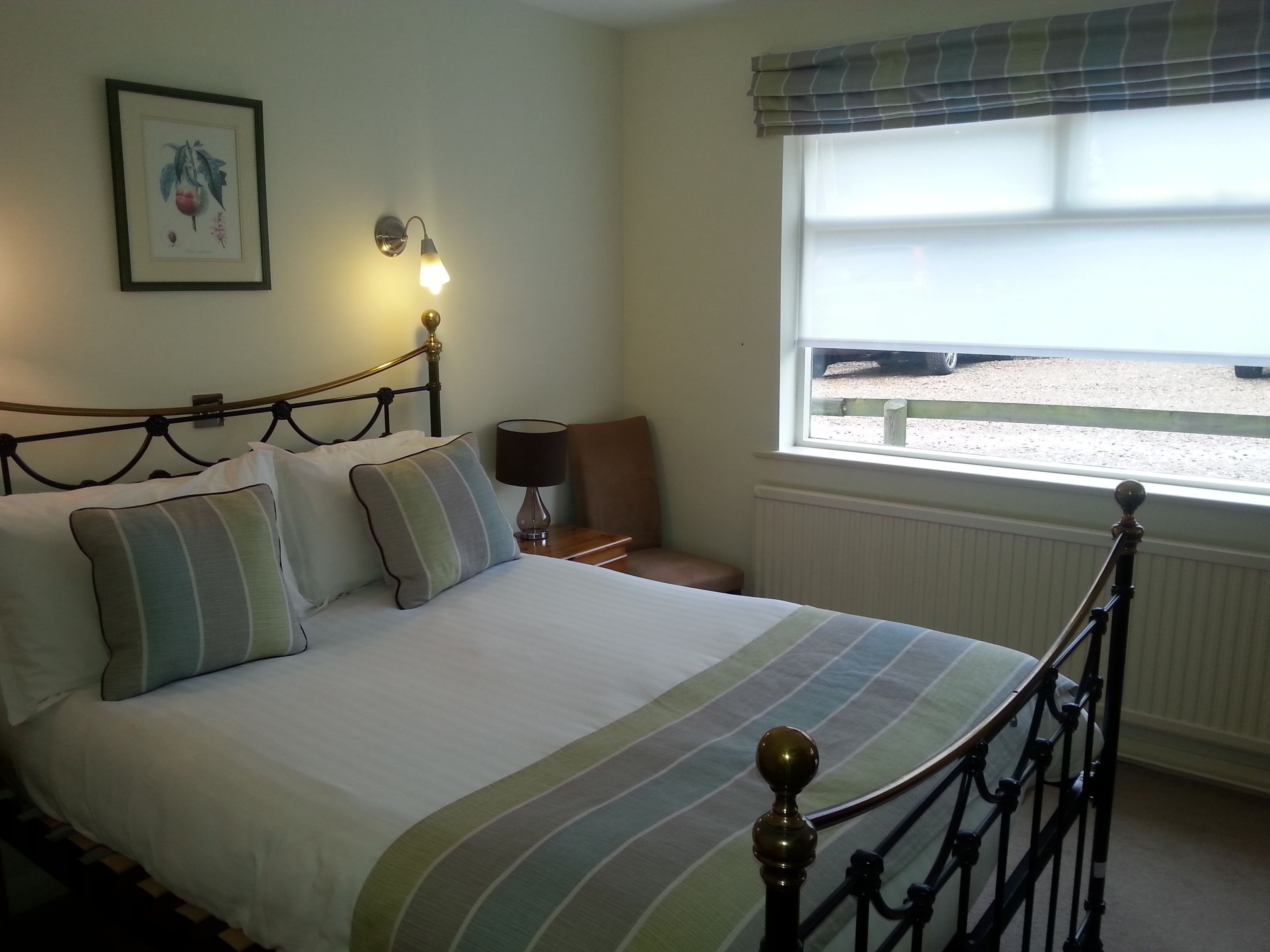 Una cama bien tendida con ropa de cama a rayas, una lámpara fijada a la pared y una ventana con vista a la playa.