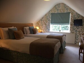 A bedroom with two beds, a television, and a window with a view of greenery. - The Marquess Of Exeter (Oakham)