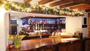 A bar area with wooden beams, a shelf of liquor bottles, and a garland of lights. - The Marquess Of Exeter (Oakham)