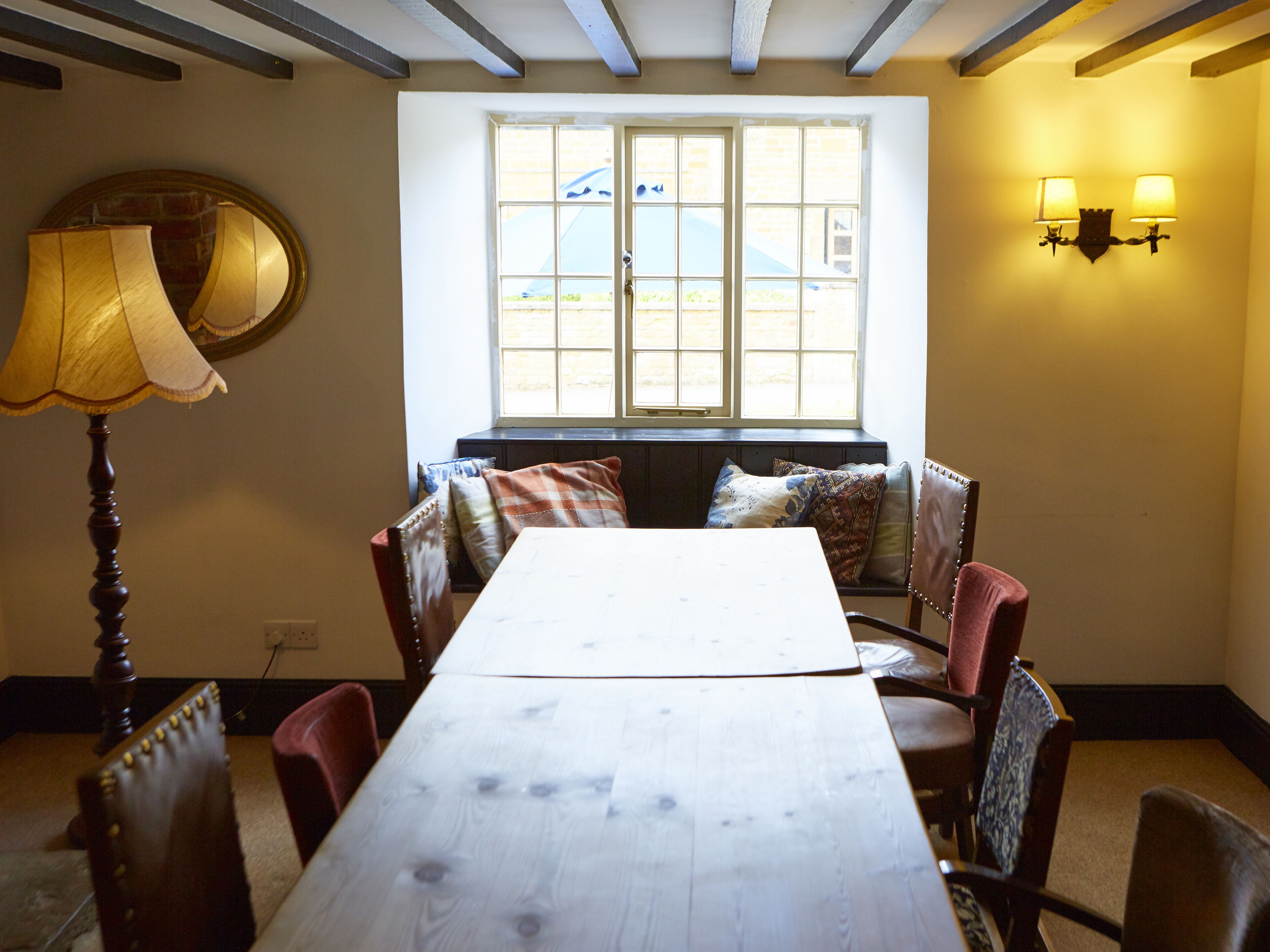 A dining area with a wooden table and chairs, a bench with cushions, a lamp, and a window with multiple panes.