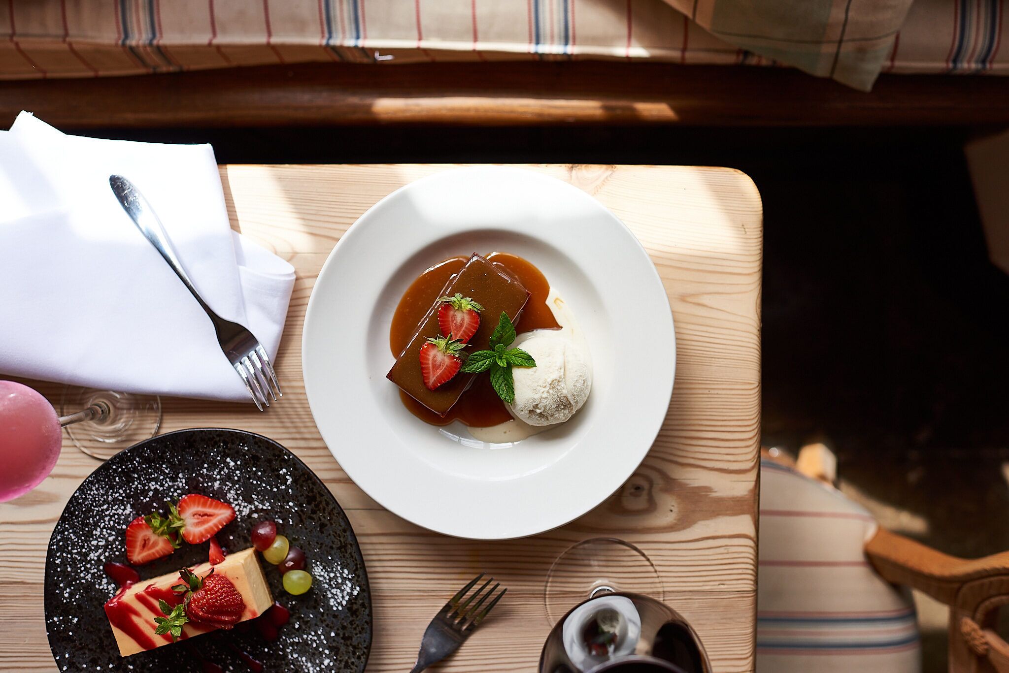 A dessert plate with a caramel dessert, strawberries, and a scoop of ice cream on a wooden table.