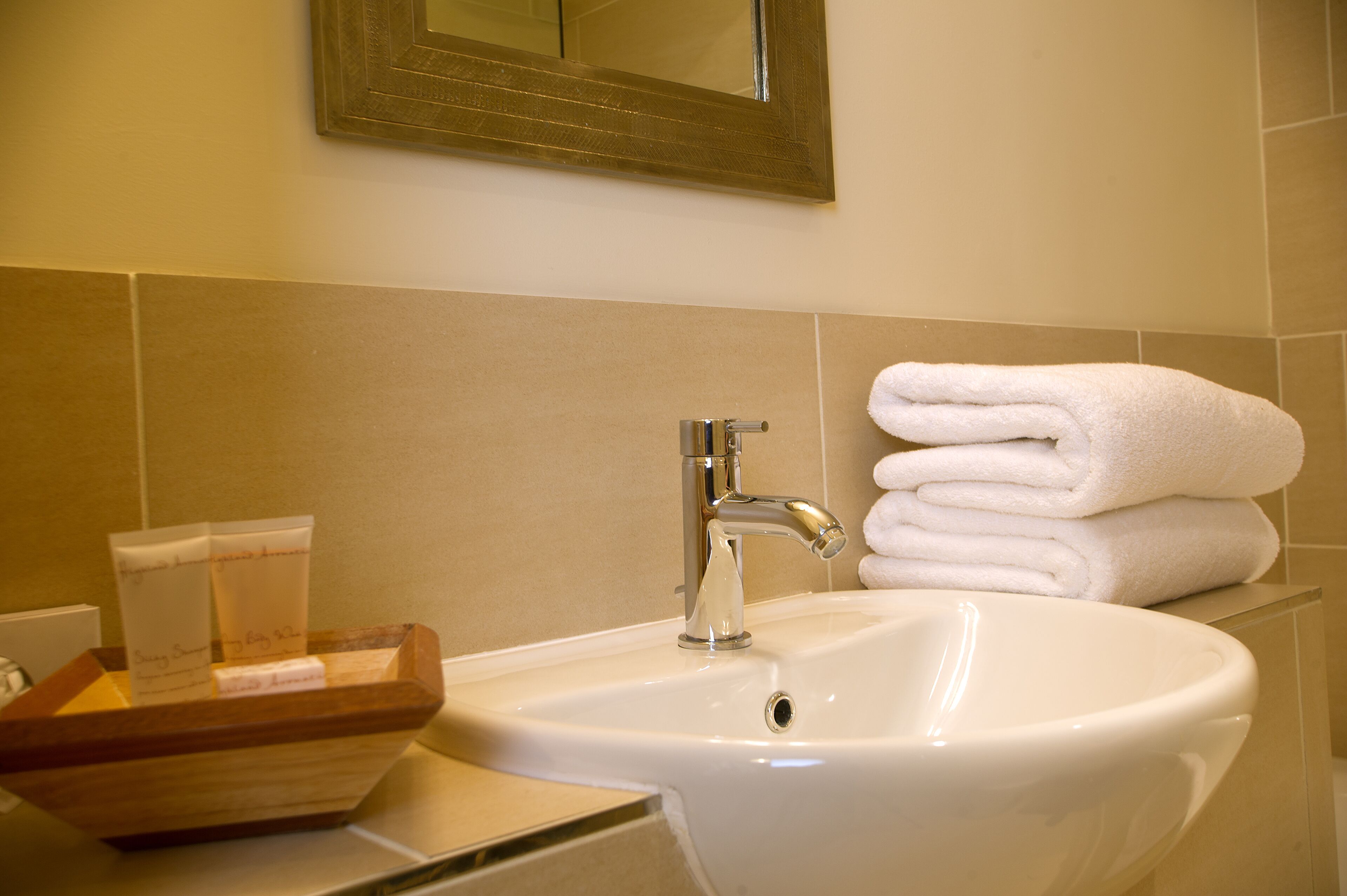A bathroom with a sink, a mirror, and a stack of white towels.