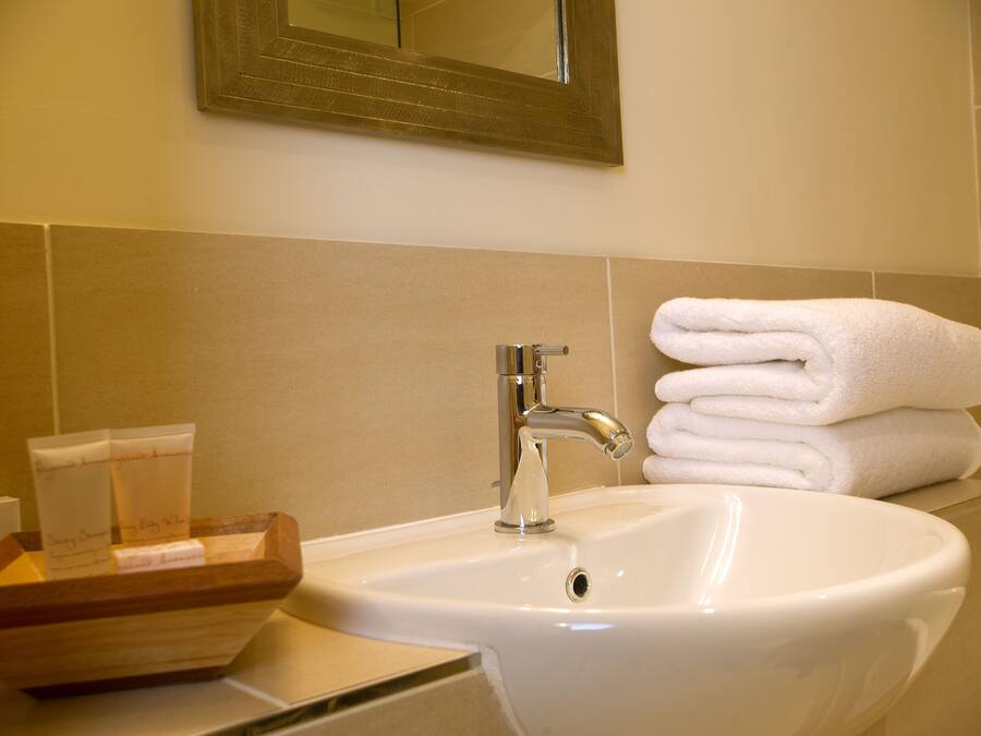 A bathroom with a sink, a mirror, and a stack of white towels.