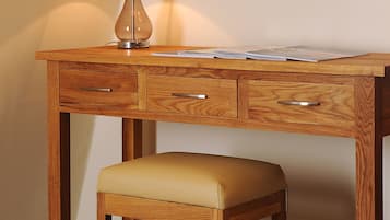 Een houten bureau met een lamp, een spiegel en een comfortabele stoel.