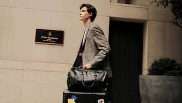 A man walking with a suitcase and a black bag, passing a sign for Four Seasons Hotel New York Downtown.
