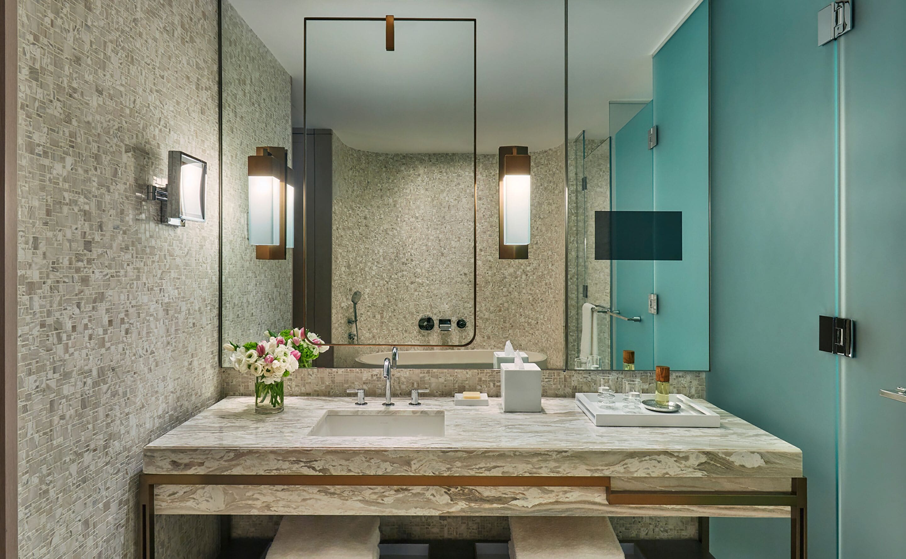 A modern bathroom with a marble sink, a large mirror, and a teal accent wall.