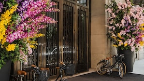 Een hotelentree met een grote bloemenpresentatie, twee fietsen en een helder zicht op de gevel.