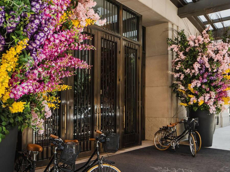 A hotel entrance with a large floral display, two bicycles, and a clear view of the building's entrance.