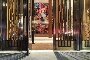 Fachada de un hotel con un mural grande, puertas metálicas y suelo alfombrado.