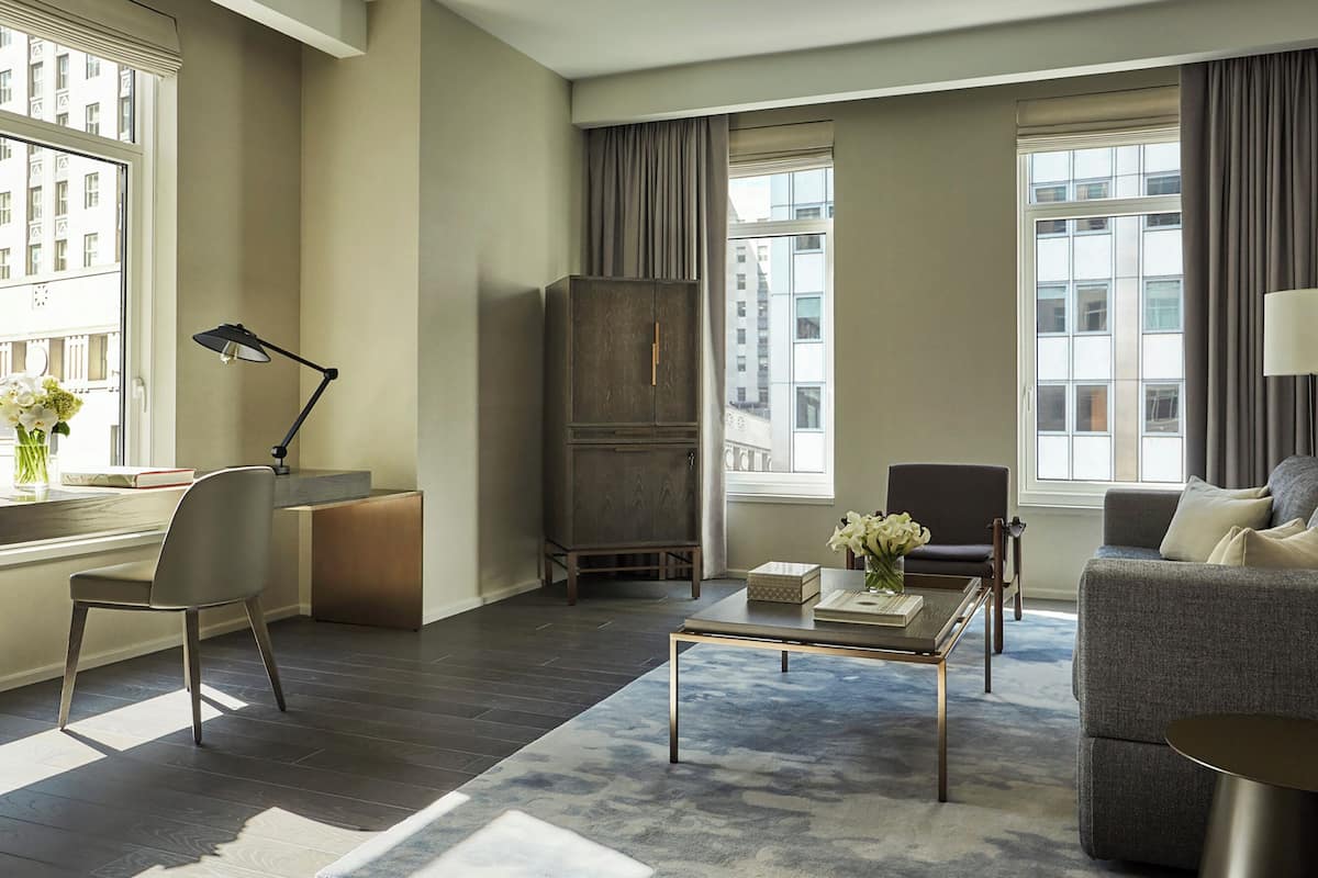 A modern living room with a sofa, armchair, coffee table, and a desk with a lamp.