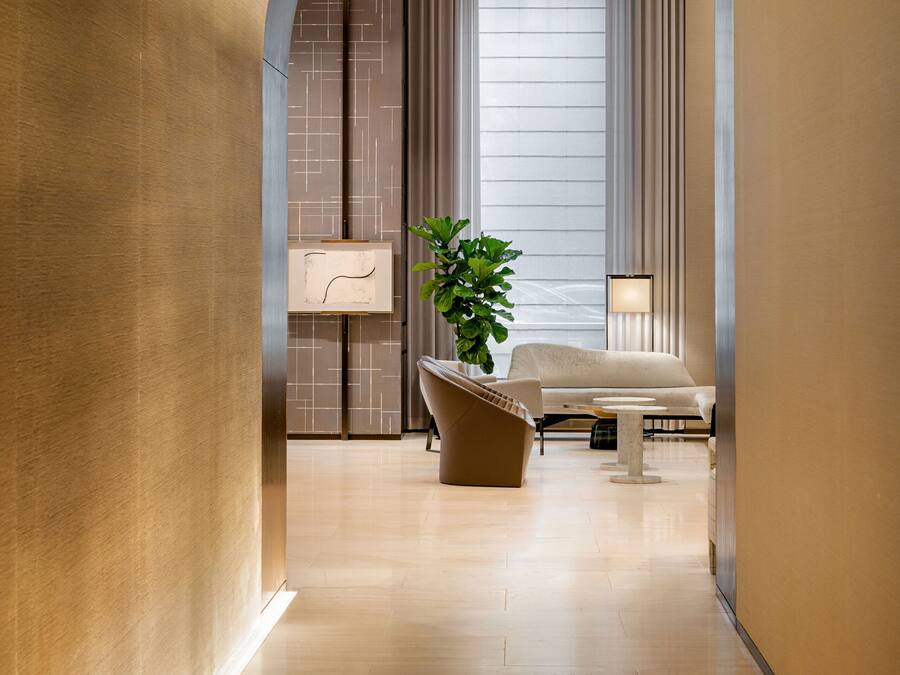 A modern hotel lobby with a wooden floor, a large potted plant, a sofa, and a lamp.
