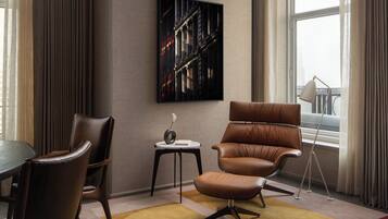 Un salon moderne avec un fauteuil en cuir marron, une petite table d’appoint sur laquelle est posé un vase, et une grande fenêtre avec des rideaux.