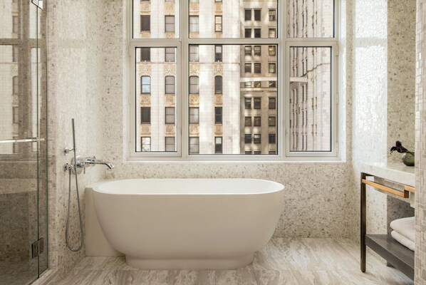 Une salle de bain moderne avec une baignoire sur pieds, une douche en verre et une grande fenêtre donnant sur un immeuble.