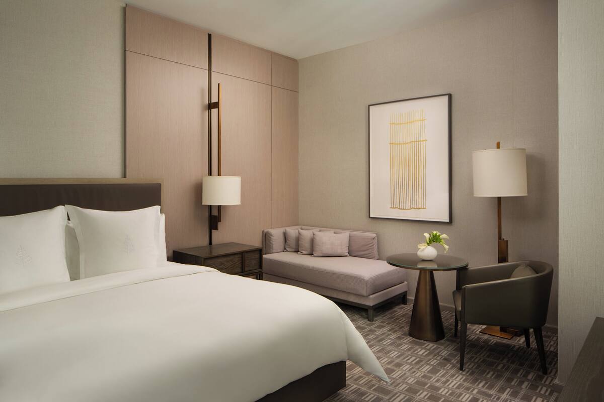 A hotel room with a large bed, a sofa, a small table with a lamp, and a chair.