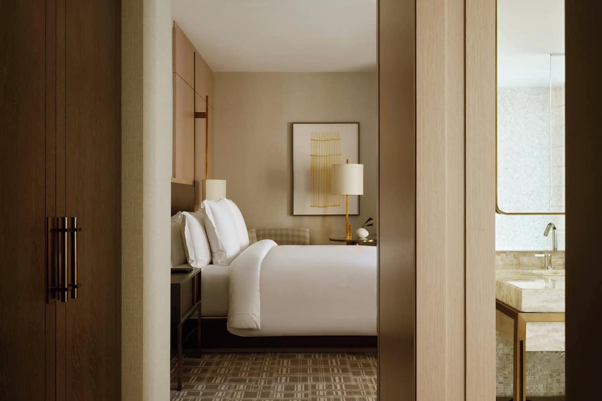 A hotel room with a bed, bedside table, lamp, and a framed artwork on the wall.