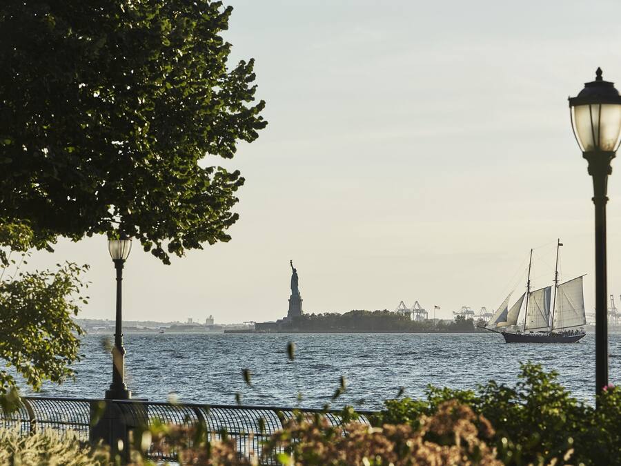 A waterfront view with a statue, a sailboat, and a lamp post.