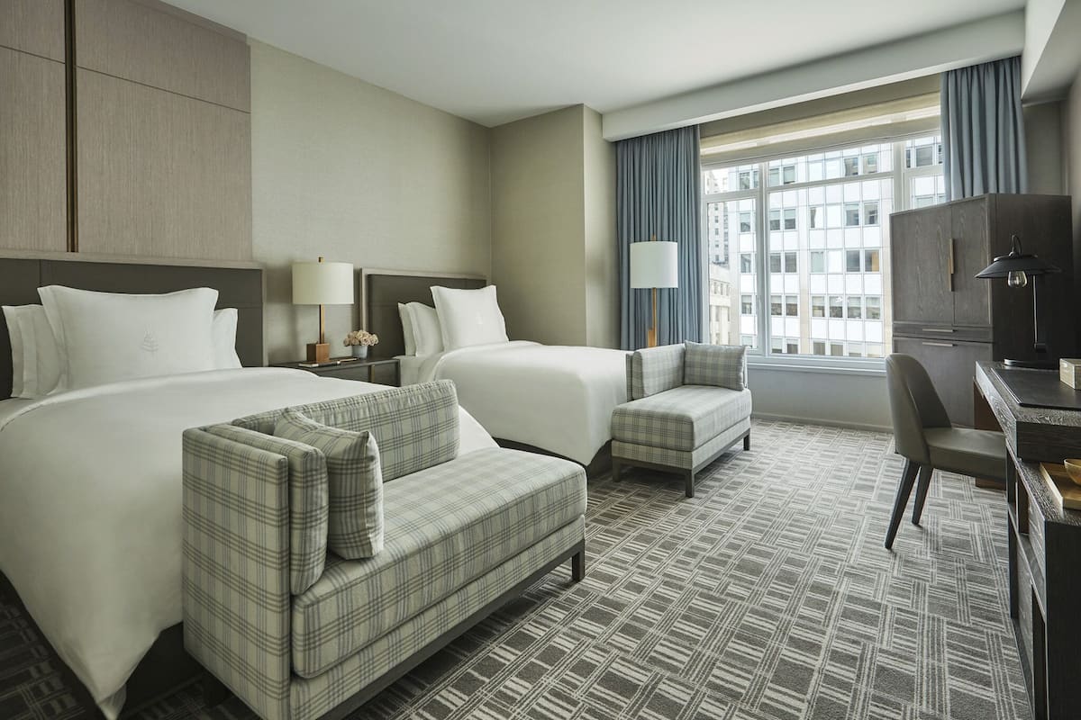 A hotel room with two beds, a sofa, a desk, and a large window with curtains.