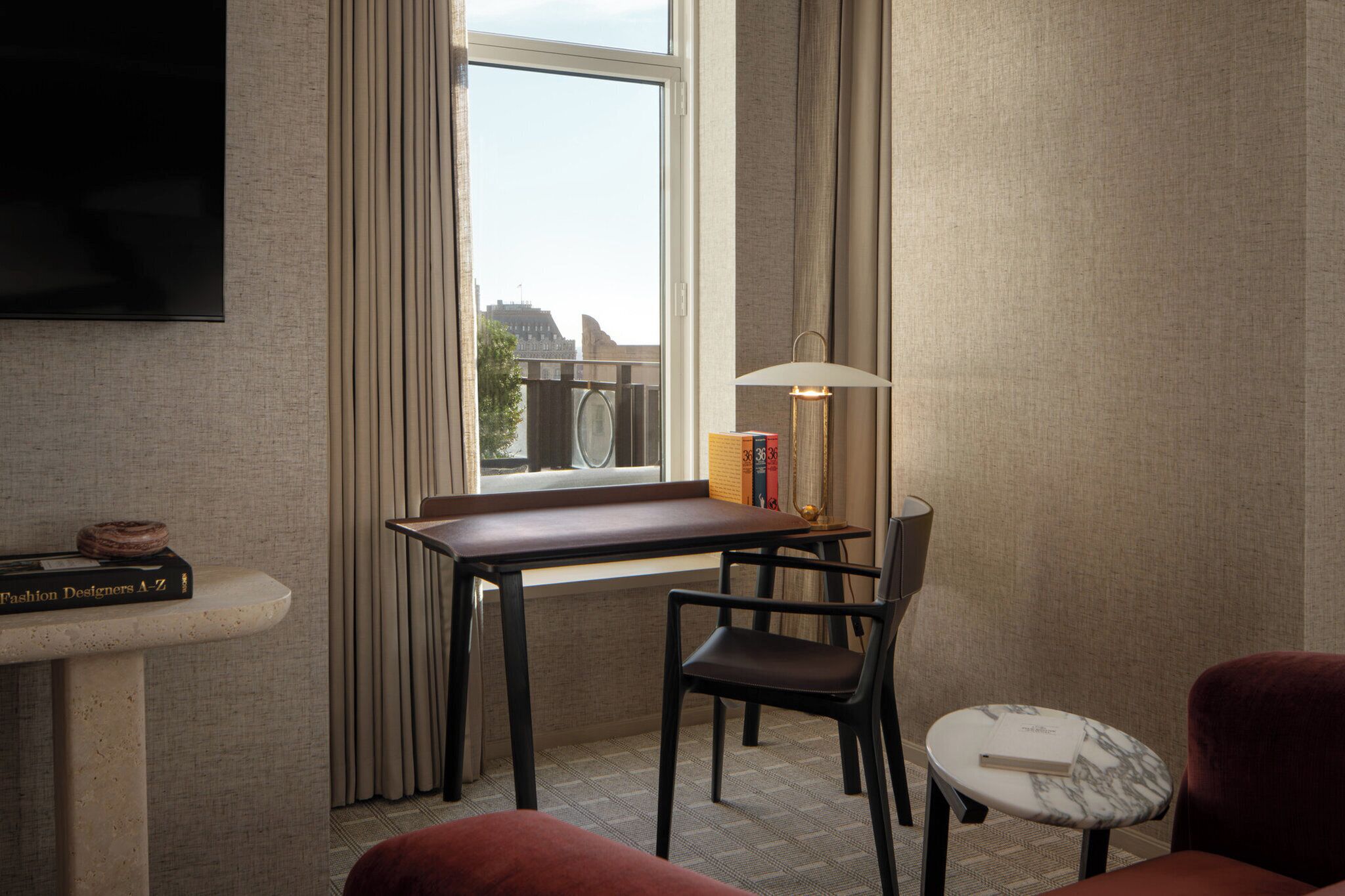A hotel room with a desk, chair, and a TV mounted on the wall.