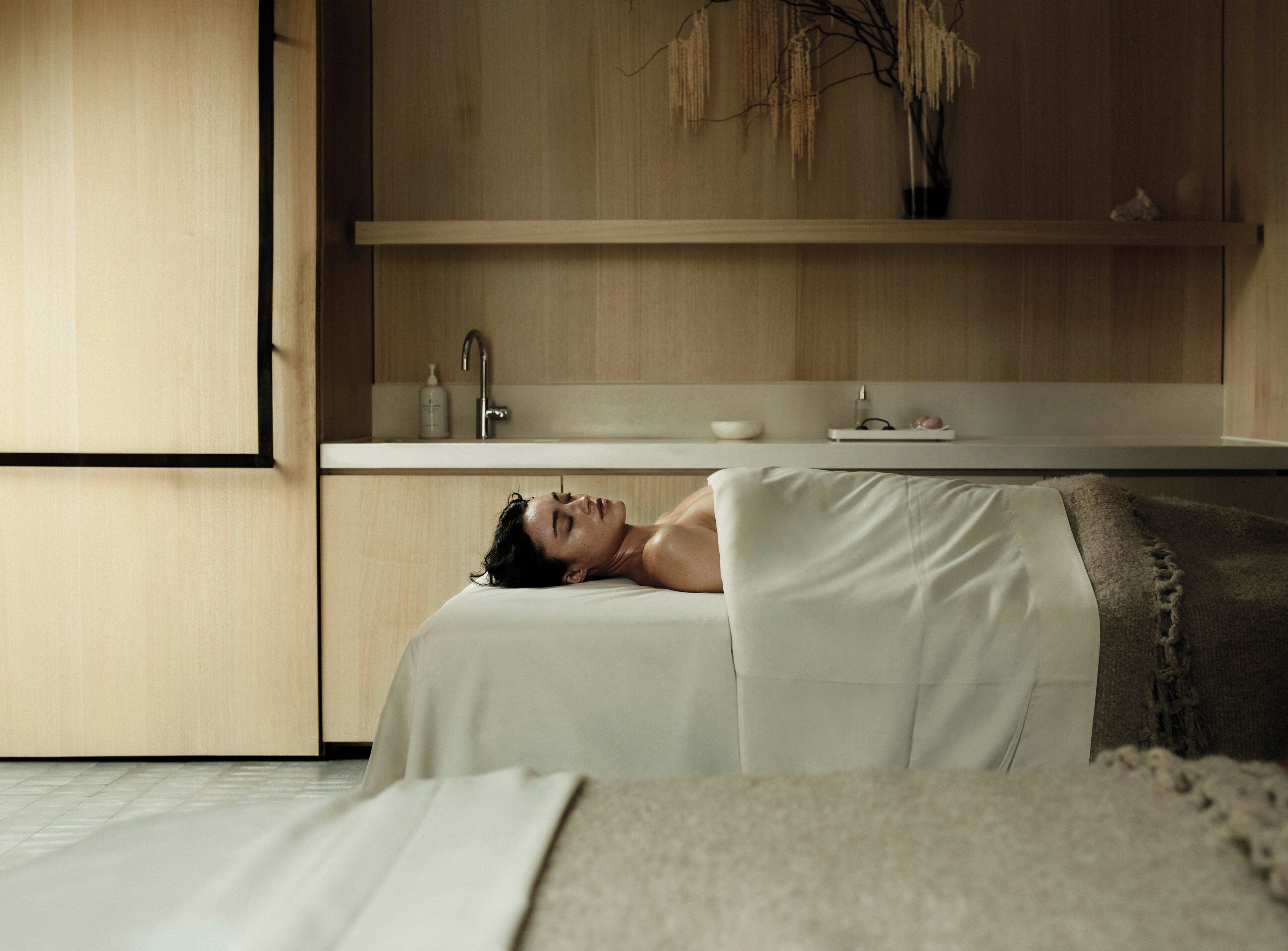 A person lying on a bed in a room with a wooden cabinet and a white countertop.