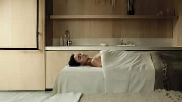 A person lying on a bed in a room with a wooden cabinet and a white countertop.