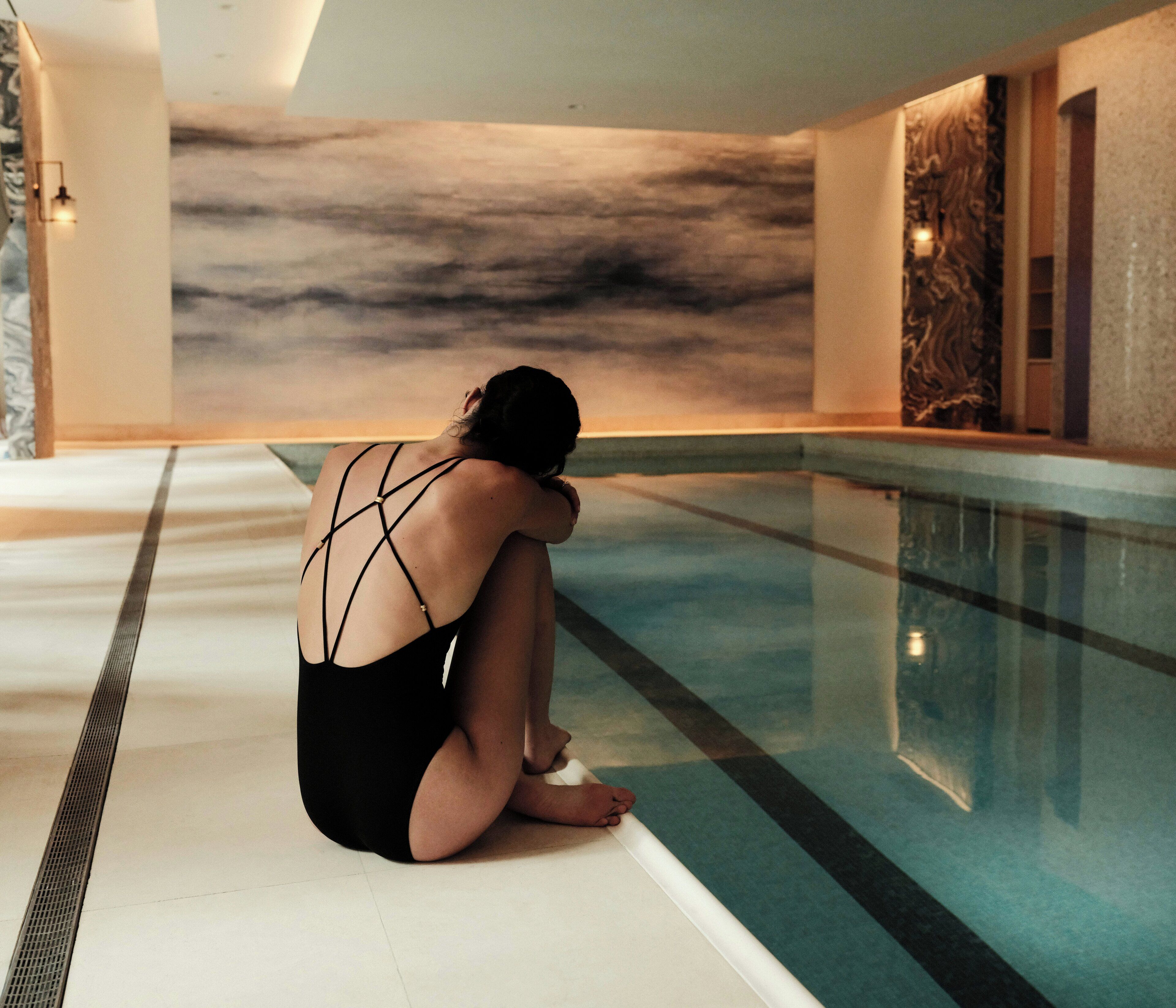 A person sitting by a pool with a marble wall in the background.