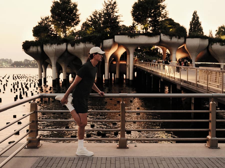 A person standing on a bridge with a railing, overlooking a body of water and trees.
