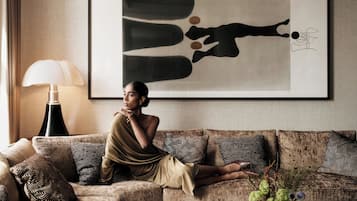 A living room with a sofa, a lamp, a framed abstract painting, and a small table with a vase of flowers.