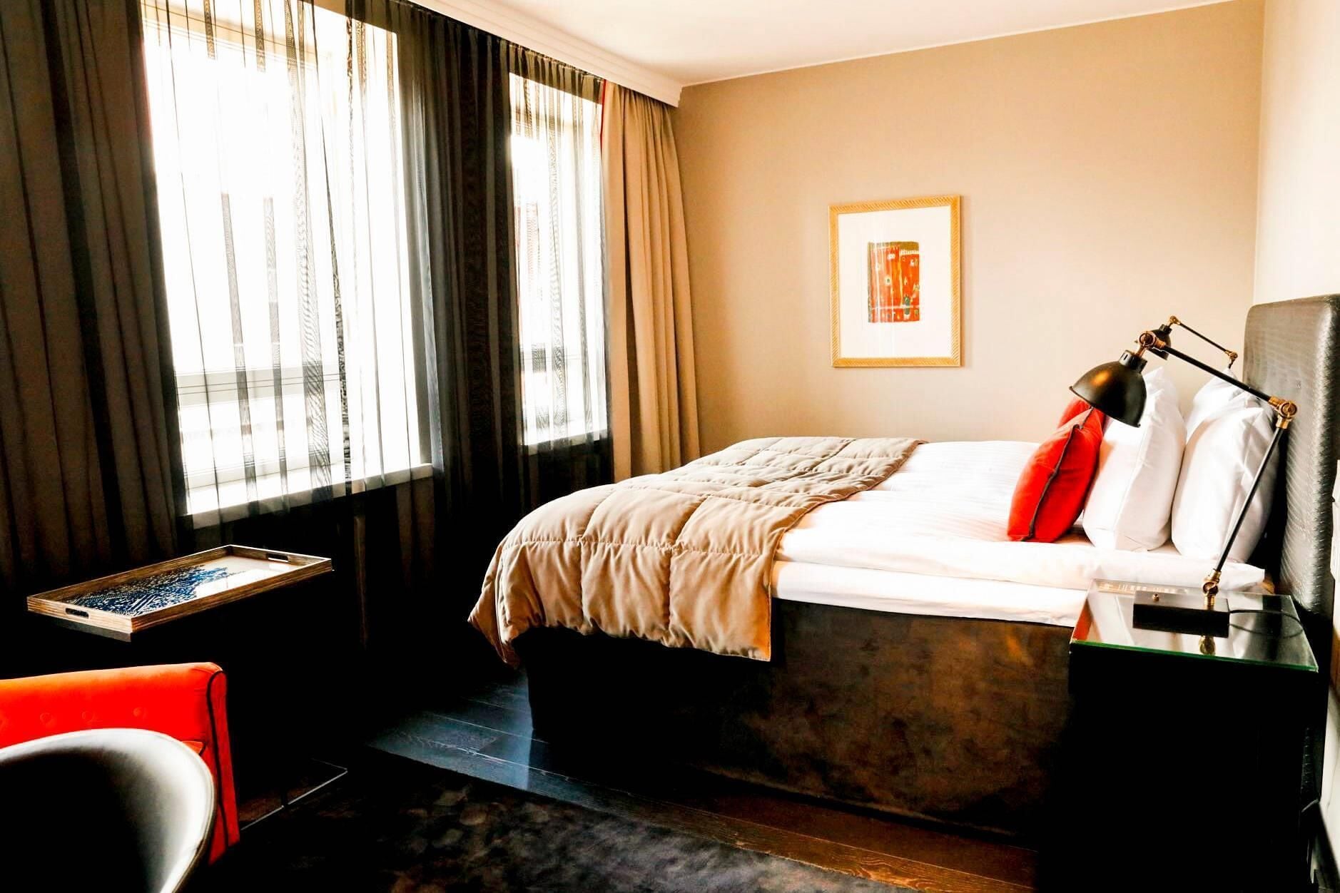 A hotel room with a bed, a desk, a chair, and a window with curtains.