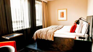 A hotel room with a bed, a desk, a chair, and a window with curtains.