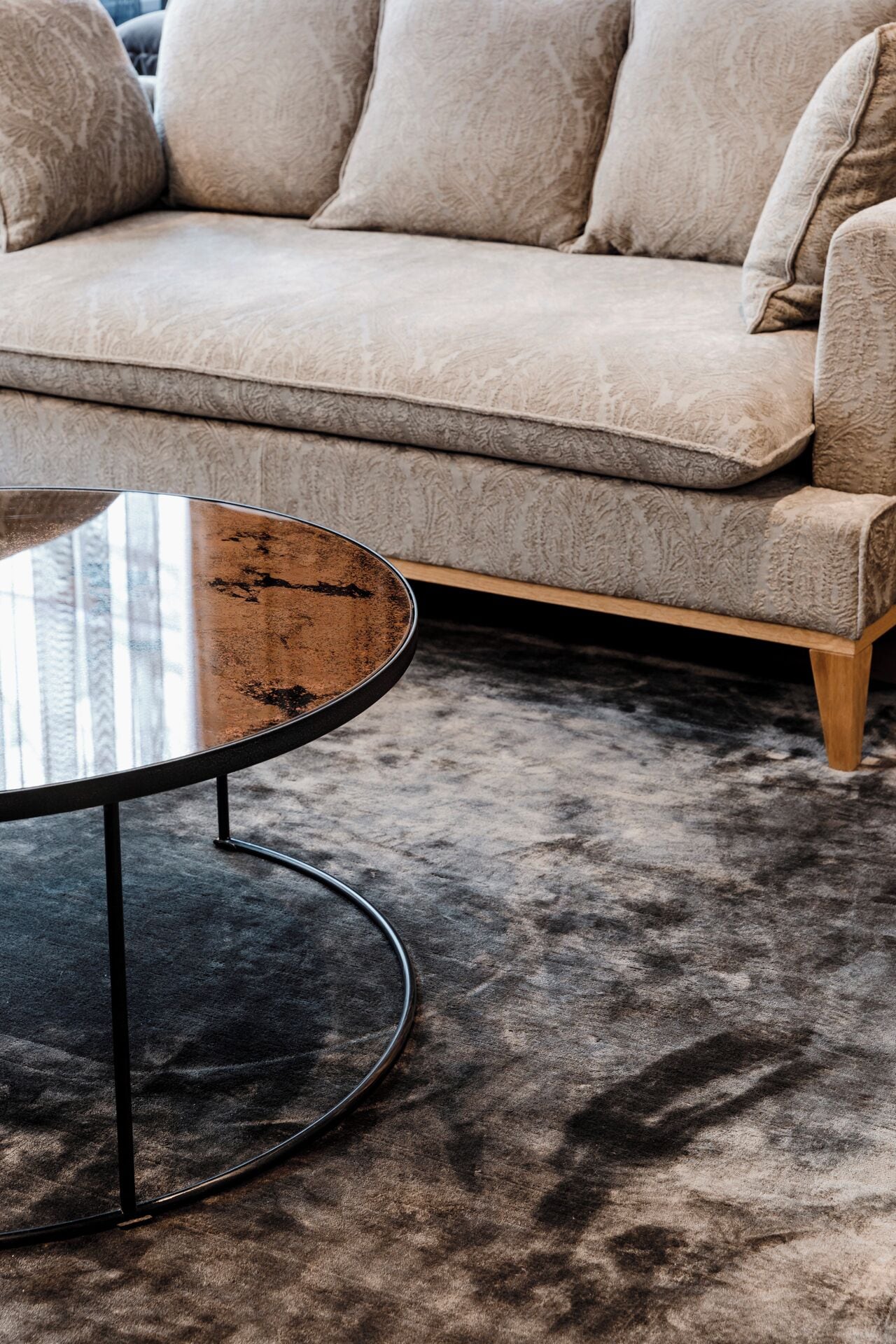 A beige sofa with a patterned fabric and a round coffee table with a metal frame.