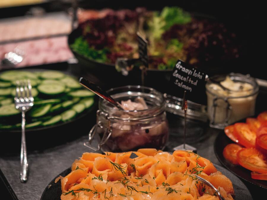 A buffet with various dishes including salmon, salad, and sliced vegetables.