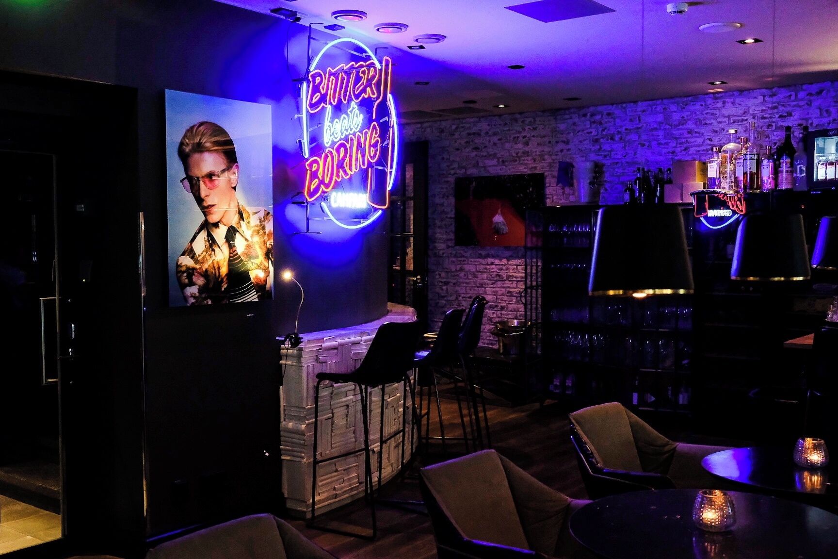 A bar area with a neon sign reading "BUTTER BEATS BORING," a DJ booth, bar stools, and a brick wall backdrop.