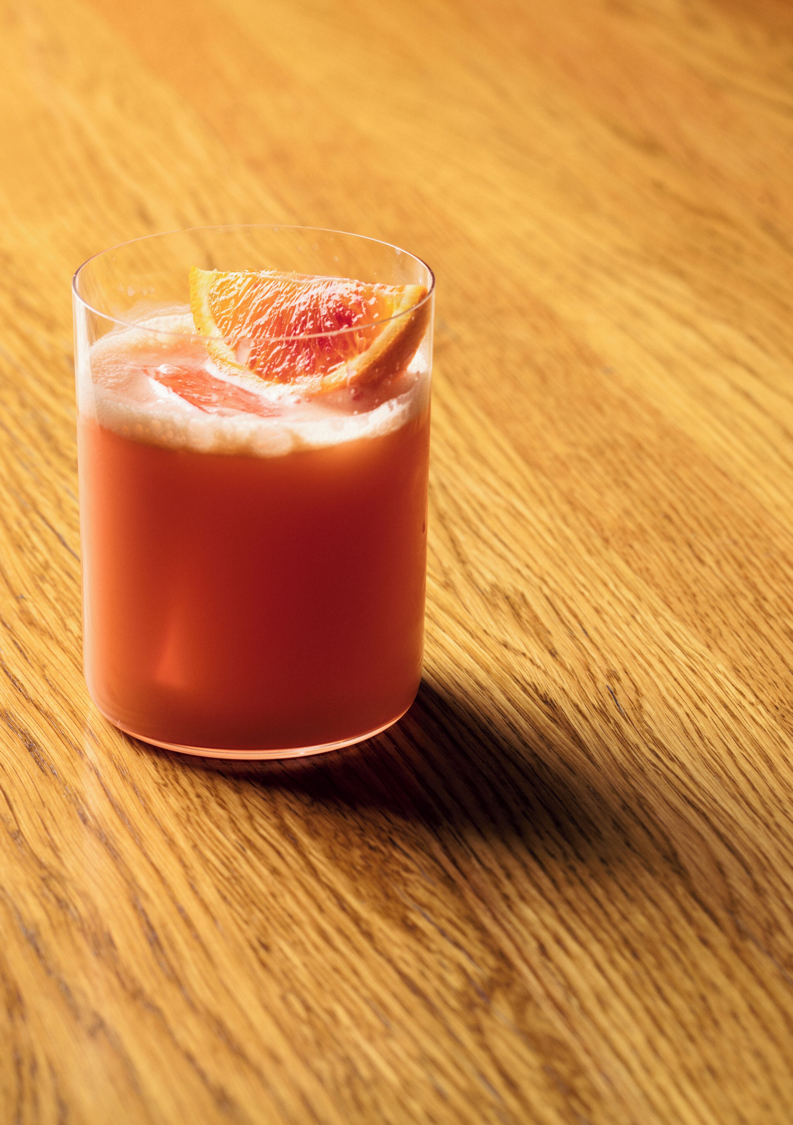 A glass of pink beverage with a slice of fruit on a wooden table.