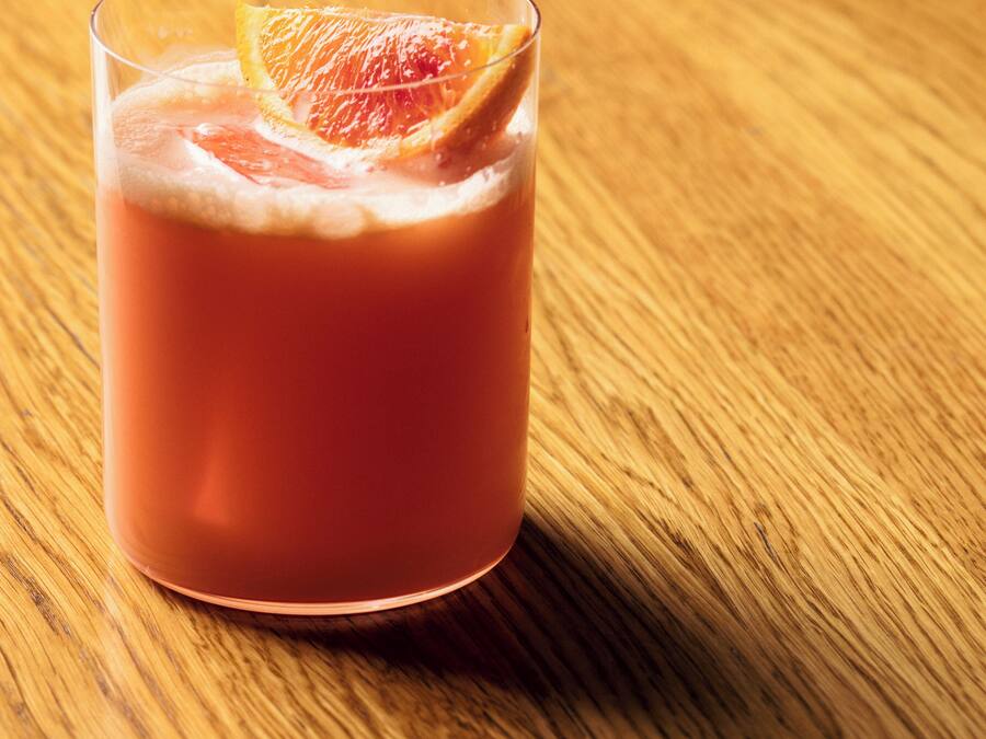 A glass of pink beverage with a slice of fruit on a wooden table.