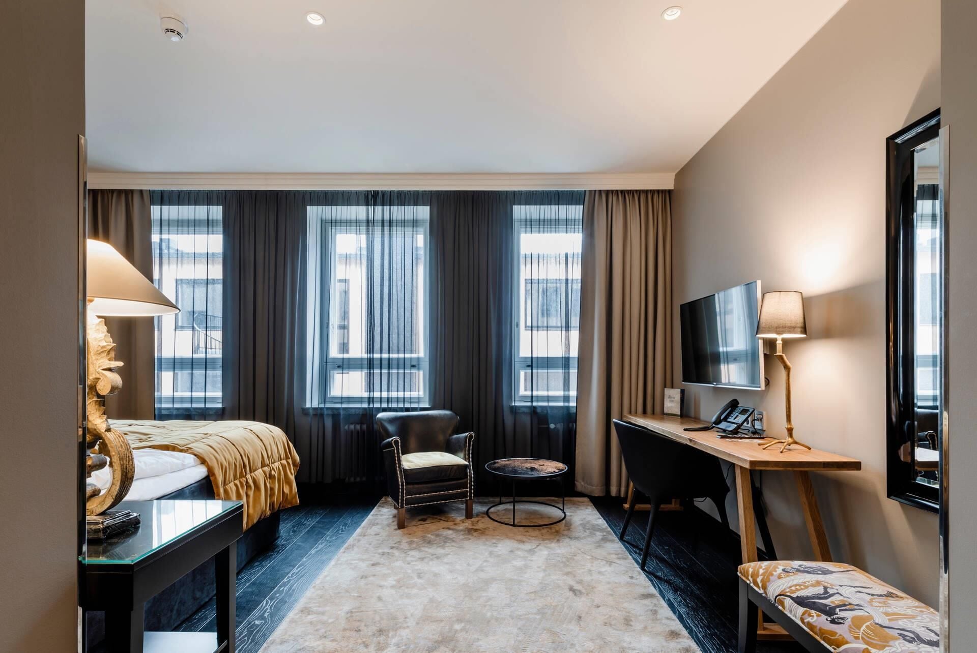 A hotel room with a bed, a desk, a chair, a TV, and a lamp.