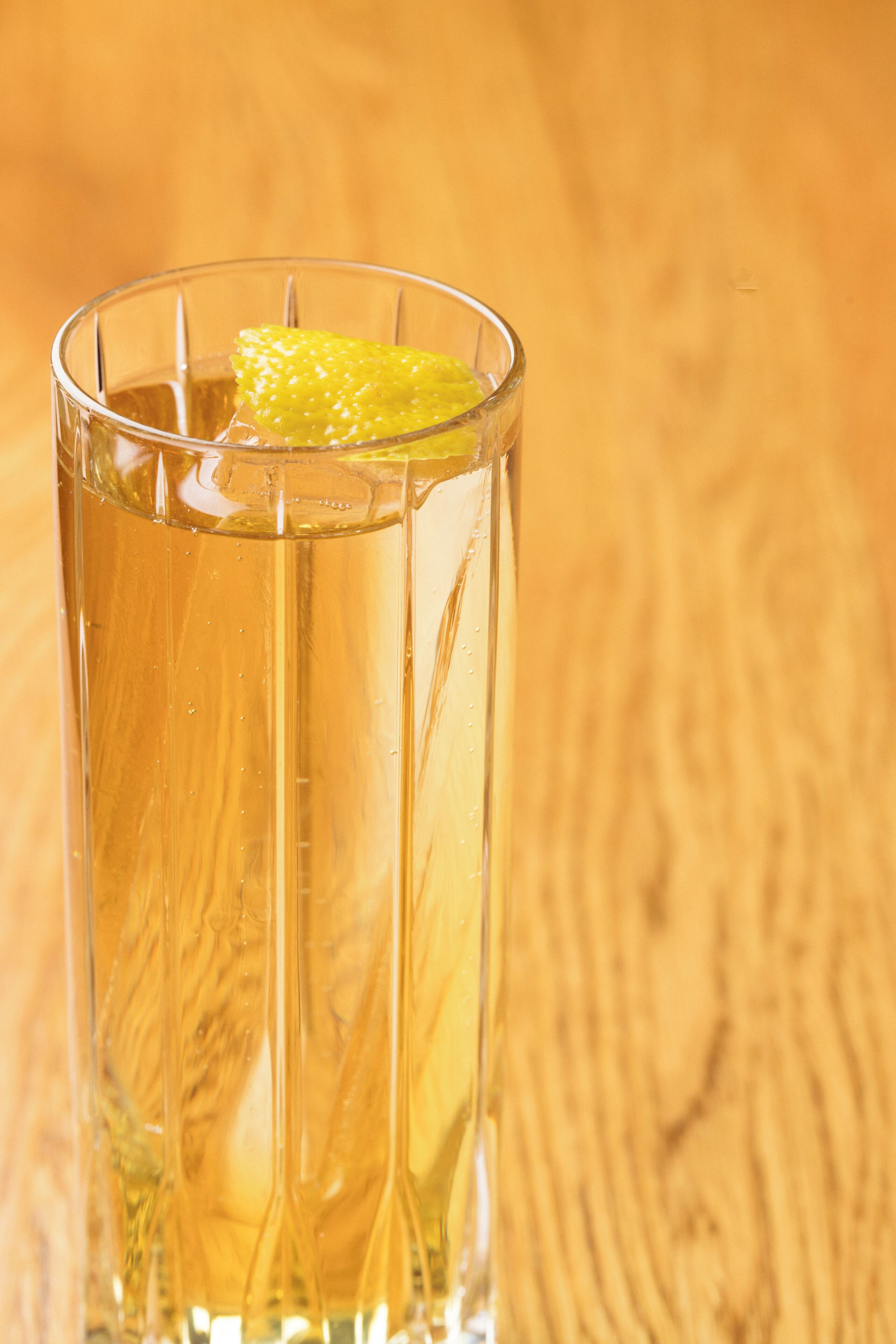 A clear glass with a yellowish liquid and a slice of lemon on a wooden surface.
