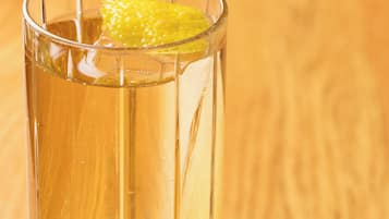 A clear glass with a yellowish liquid and a slice of lemon on a wooden surface.