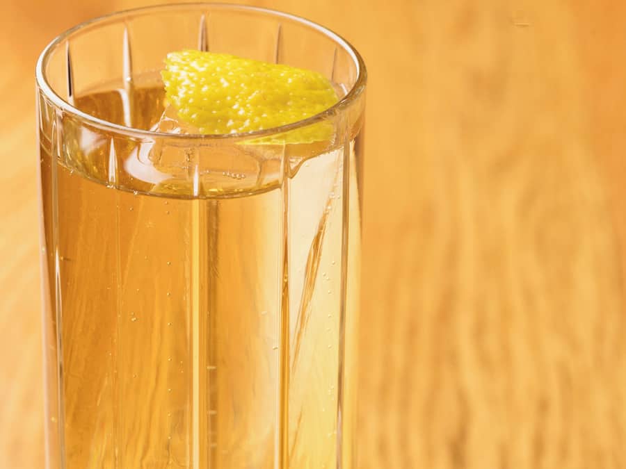 A clear glass with a yellowish liquid and a slice of lemon on a wooden surface.