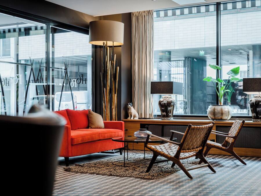 A modern living room with a red sofa, two armchairs, a coffee table, and a large window with curtains.