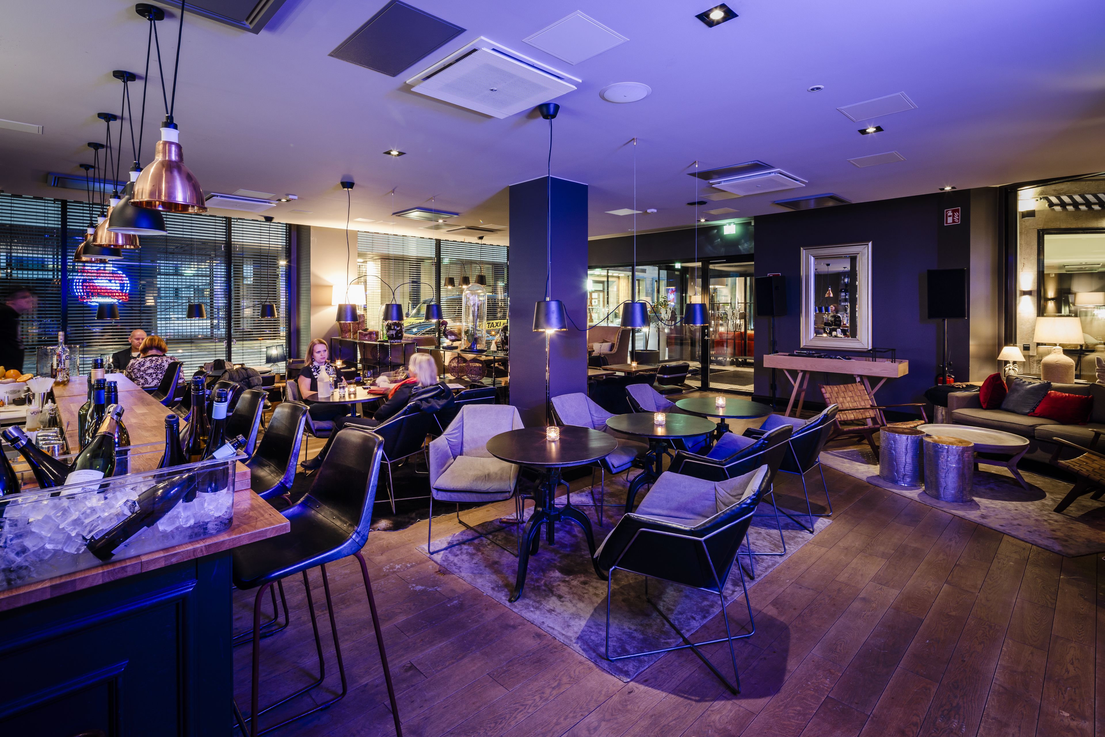 A modern bar area with seating and a bar counter, featuring ice, bottles, and glasses.