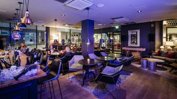 A modern bar area with seating and a bar counter, featuring ice, bottles, and glasses.