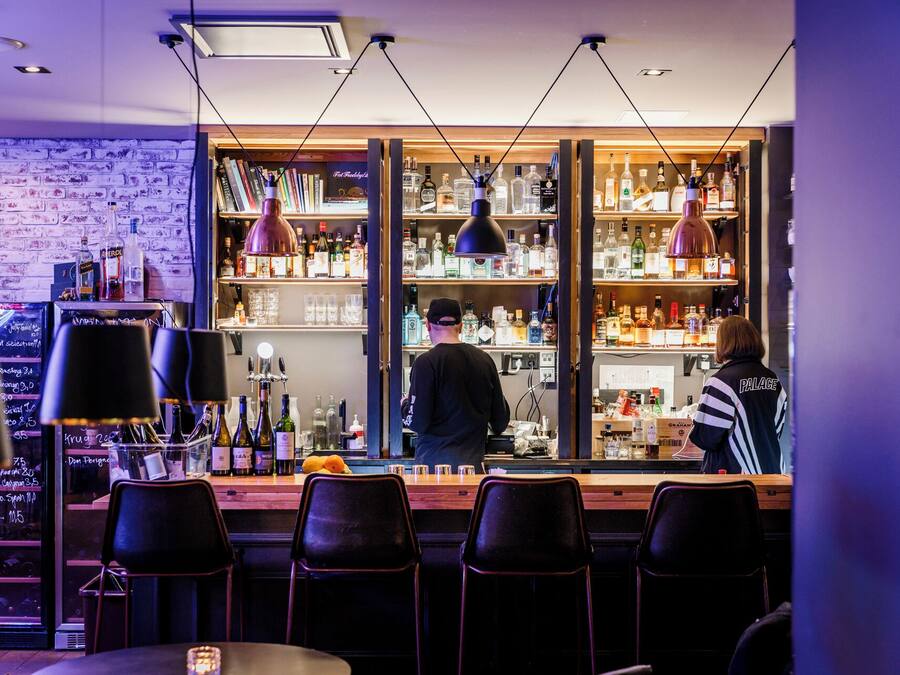 Eine Bar mit einer Ziegelwand, Regalen voller Spirituosenflaschen und Barhocker.