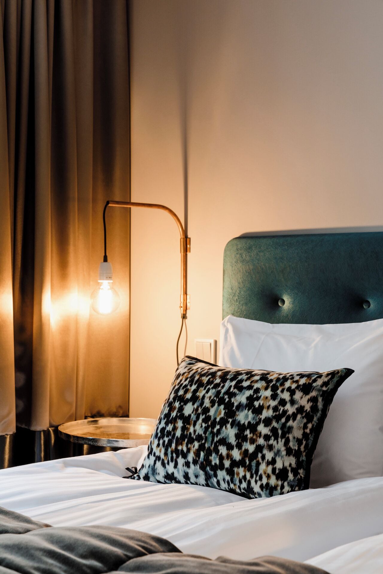 Una cama impecablemente tendida con sábanas blancas, un cojín estampado y un cabecero tapizado en verde.